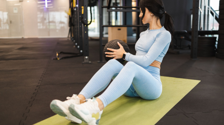 Long-haired person in gym doing ab exercise with medicine ball
